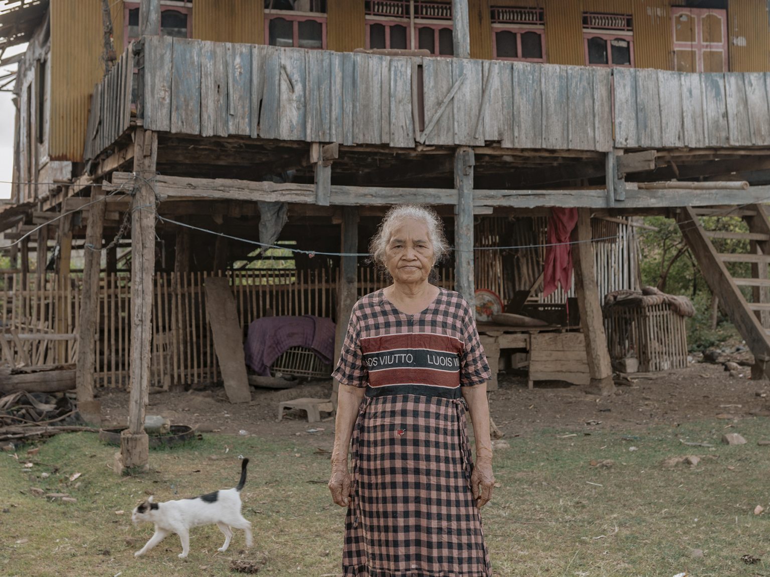 Raba Intang, 80, stands in front of the house she no longer lives in. She moved to her child’s home because she could no longer endure the deafening noise and the sulfur stench from nearby smelters. Even there, dust still drifts in, forcing her to sweep up to 15 times a day.